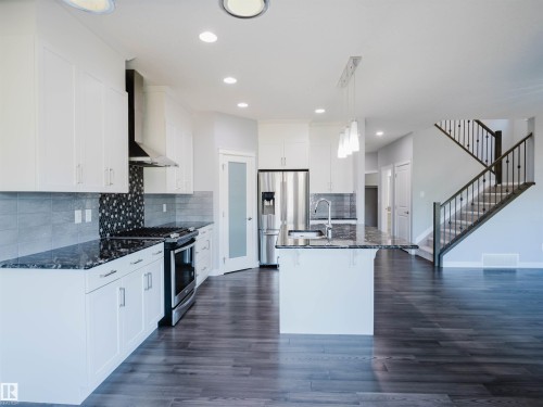 Contemporary kitchen featuring white cabinetry, dark stone countertops, stainless steel appliances, and a central island with a sink - 2526 Wonnacott Loop, Edmonton, AB 