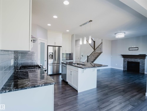 Open-concept kitchen and living area featuring white cabinetry, dark stone countertops, and stainless steel appliances - 2526 Wonnacott Loop, Edmonton, AB 