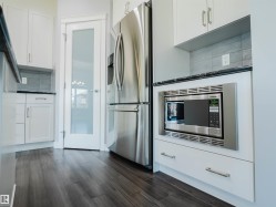 Kitchen featuring white cabinetry, stainless steel appliances, dark wood-finish flooring, dark countertops, and a light gray tile backsplash - 
