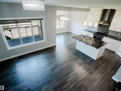Expansive open-concept living area featuring wood-finish flooring, a contemporary kitchen island with a dark stone countertop, white cabinetry, and a mosaic tile backsplash - 2526 Wonnacott Loop, Edmonton, AB 