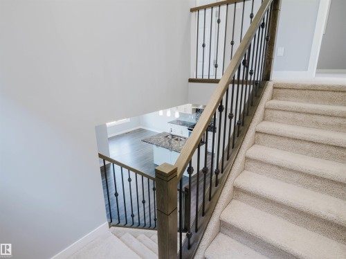 Carpeted staircase featuring a light wood-finish handrail and black metal balusters - 2526 Wonnacott Loop, Edmonton, AB 