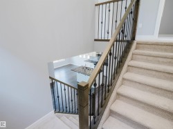 Carpeted staircase featuring a light wood-finish handrail and black metal balusters - 