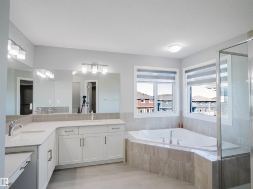 Corner soaking tub with tile surround, dual vanity with white cabinetry, light countertops, and large framed mirrors - 2526 Wonnacott Loop, Edmonton, AB 