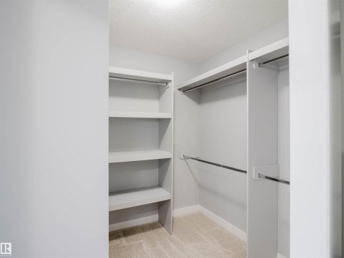 Walk-in closet featuring built-in shelving, multiple hanging rods, and neutral carpet flooring - 2526 Wonnacott Loop, Edmonton, AB 