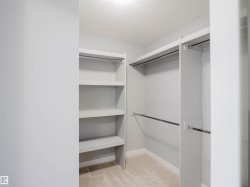 Walk-in closet featuring built-in shelving, multiple hanging rods, and neutral carpet flooring - 