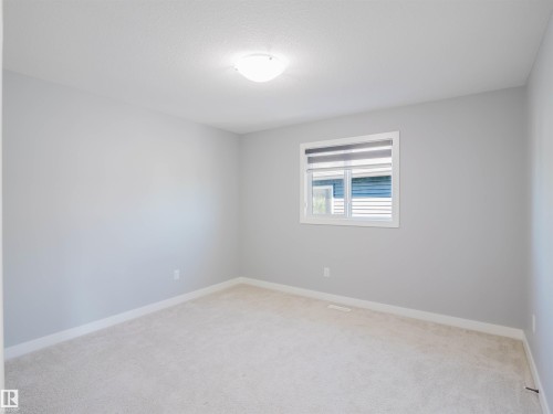 Neutral-toned room featuring a single window with blinds, light-colored carpeting, white baseboards, and a ceiling-mounted light fixture - 2526 Wonnacott Loop, Edmonton, AB 