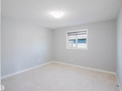 Neutral-toned room featuring a single window with blinds, light-colored carpeting, white baseboards, and a ceiling-mounted light fixture - 