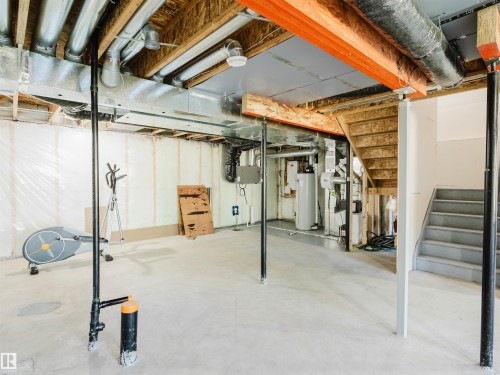 Unfinished basement space featuring a concrete floor, exposed ceiling joists and ductwork, a visible water heater, and an unfinished staircase - 2526 Wonnacott Loop, Edmonton, AB 
