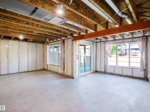 Unfinished basement featuring exposed wood joists and subfloor, concrete flooring, spray foam insulation, multiple windows, and a sliding glass door - 2526 Wonnacott Loop, Edmonton, AB 