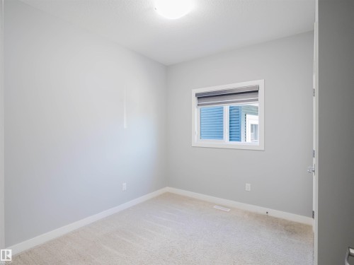 Neutral-toned room featuring a single window with a privacy blind, light-colored carpeting, white baseboards, and a flush-mount ceiling light - 2526 Wonnacott Loop, Edmonton, AB 