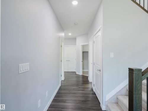 Hallway featuring wood-finish flooring, recessed lighting, neutral wall paint, white trim, and doors with brushed nickel hardware - 2526 Wonnacott Loop, Edmonton, AB 