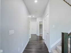 Hallway featuring wood-finish flooring, recessed lighting, neutral wall paint, white trim, and doors with brushed nickel hardware - 