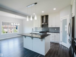 Modern kitchen featuring an island with a dark countertop, white cabinetry, stainless steel appliances, and wood-finish flooring - 