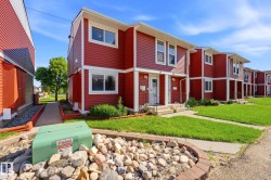 Red-sided multi-unit residence featuring white window trim, white soffits, and a concrete pathway - 