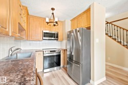 Kitchen featuring wood cabinetry, stainless steel appliances, a white tile backsplash, and stone-finish countertops - 