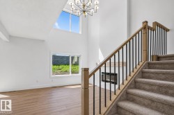 Two-story entry featuring a modern chandelier and a carpeted staircase with wood and metal railings - 