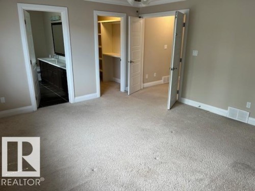 Carpeted interior space featuring a bathroom with a dark wood-finish vanity and integrated sink, a walk-in closet with built-in shelving, white trim, and light beige walls - 805 Hodgins Road, Edmonton, AB 