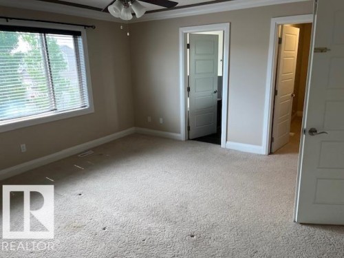 Carpeted interior space featuring a ceiling fan with integrated lighting, a large window with blinds, and white trim throughout - 805 Hodgins Road, Edmonton, AB 