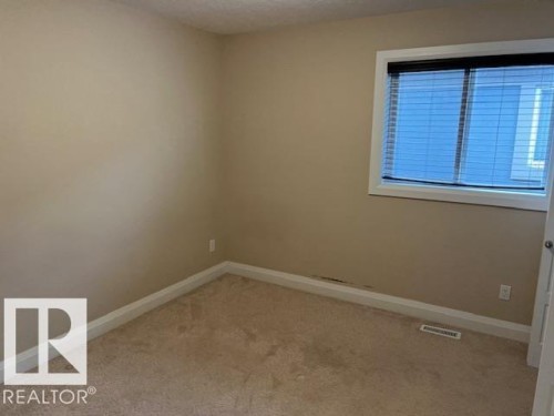 Carpeted room featuring a single window with blinds, baseboard trim, and a wall vent - 805 Hodgins Road, Edmonton, AB 