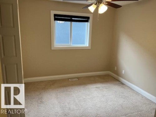 Carpeted room featuring a ceiling fan with integrated lighting, a paneled door, and a window with white trim and a black roller blind - 805 Hodgins Road, Edmonton, AB 