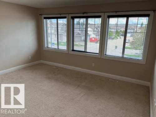 Light beige carpeted room featuring three large windows with white trim and horizontal blinds - 805 Hodgins Road, Edmonton, AB 