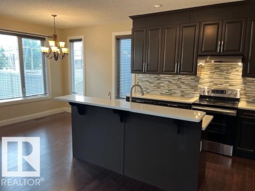 Kitchen featuring dark wood-finish cabinetry, light-toned countertops, and a full tile backsplash - 805 Hodgins Road, Edmonton, AB 
