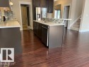 Open-concept kitchen featuring dark wood cabinetry, white countertops, stainless steel appliances, a multi-tone tile backsplash, and wood-finish flooring - 805 Hodgins Road, Edmonton, AB 