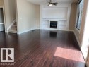 Spacious living area featuring rich wood-finish flooring, a built-in fireplace with a decorative mantel, integrated shelving, and a ceiling fan - 805 Hodgins Road, Edmonton, AB 