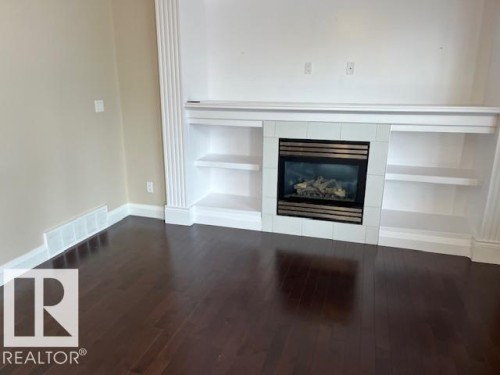 Built-in fireplace with tile surround, integrated shelving, dark wood-finish flooring, and white baseboards - 805 Hodgins Road, Edmonton, AB 