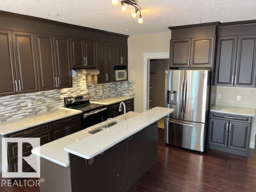 Modern kitchen featuring rich cabinetry, light countertops, and a full suite of stainless steel appliances - 805 Hodgins Road, Edmonton, AB 