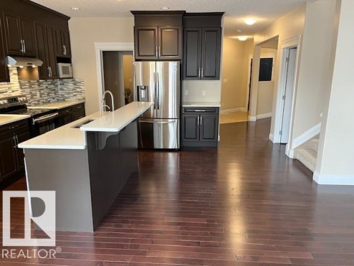 Kitchen featuring dark cabinetry, stainless steel appliances, a tile backsplash, and a central island with a sink and white countertop - 805 Hodgins Road, Edmonton, AB 
