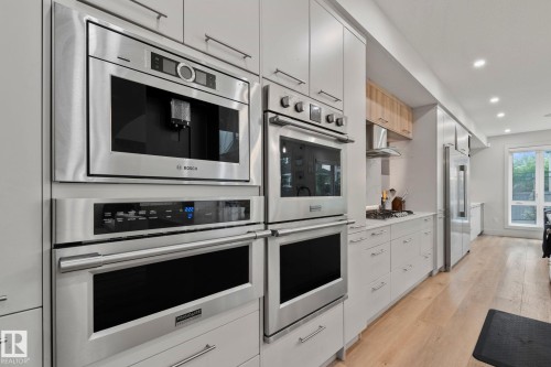 Gourmet kitchen featuring a built-in coffee maker, double wall ovens, integrated refrigerators, white shaker cabinetry, and light wood-finish flooring - 4509 Wingfield Bay Bay, Edmonton, AB 