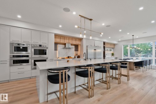 Contemporary kitchen featuring an oversized island with seating, integrated stainless steel appliances, light wood-finish flooring, full-height cabinetry, and recessed lighting - 4509 Wingfield Bay Bay, Edmonton, AB 