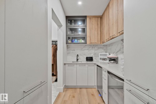 Galley-style utility space featuring wood-finish flooring, white flat-panel cabinetry, and a black faucet - 4509 Wingfield Bay Bay, Edmonton, AB 