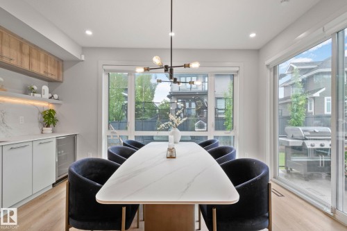 Open-concept dining area featuring a modern linear chandelier, light wood-finish flooring, and a built-in beverage refrigerator - 4509 Wingfield Bay Bay, Edmonton, AB 