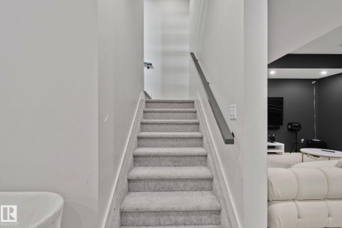 Carpeted staircase with light gray carpeting and a dark gray wall-mounted handrail - 4509 Wingfield Bay Bay, Edmonton, AB 