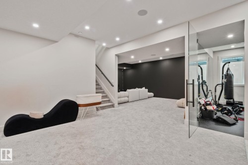 Carpeted lower level recreation space featuring recessed lighting, a glass-enclosed room with rubberized flooring, and a staircase with a dark handrail - 4509 Wingfield Bay Bay, Edmonton, AB 