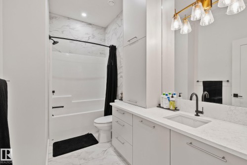 Bathroom featuring a tub and shower combination with matte black fixtures, marble-look wall tiling, and an integrated ceiling light - 4509 Wingfield Bay Bay, Edmonton, AB 