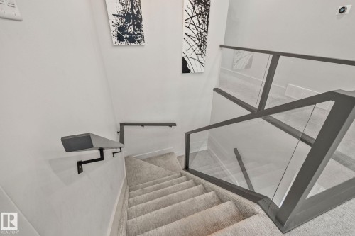 Modern staircase featuring carpeted treads, clear glass railing panels, and a contrasting dark gray handrail - 4509 Wingfield Bay Bay, Edmonton, AB 