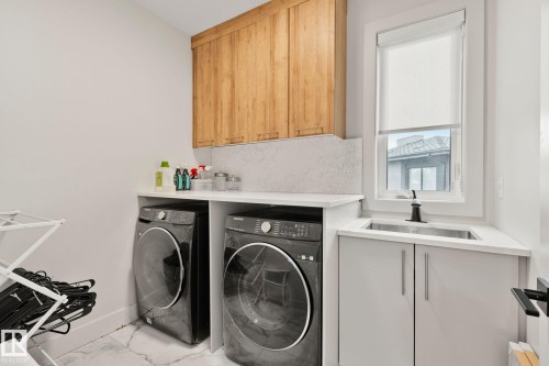 Laundry area featuring wood-finish upper cabinetry, white countertops, and a utility sink with a black faucet - 4509 Wingfield Bay Bay, Edmonton, AB 