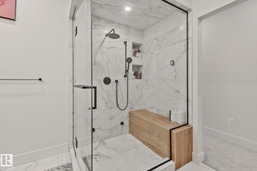 Spacious walk-in shower featuring glass enclosure with black framing, full-height marble-look tile, built-in wooden bench, dual shower heads with matte black fixtures, and recessed shelving - 4509 Wingfield Bay Bay, Edmonton, AB 