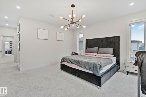 Spacious bedroom featuring light-colored carpeting, a contemporary sputnik chandelier, recessed lighting, and multiple windows providing ample natural light - 4509 Wingfield Bay Bay, Edmonton, AB 