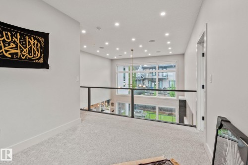 Upper-level hallway featuring light-colored carpeting, a glass and metal railing system, extensive recessed lighting, a contemporary chandelier, and large windows offering exterior views - 4509 Wingfield Bay Bay, Edmonton, AB 