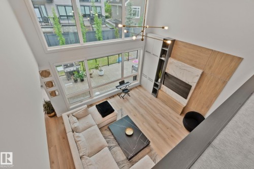 Two-story living area featuring extensive natural light, wood-finish flooring, and a contemporary fireplace with a stone and wood panel surround - 4509 Wingfield Bay Bay, Edmonton, AB 