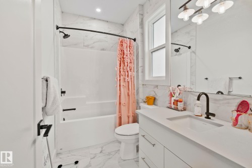 Bathroom featuring a white vanity with an integrated sink, black hardware, window, and a white tub with a shower - 4509 Wingfield Bay Bay, Edmonton, AB 
