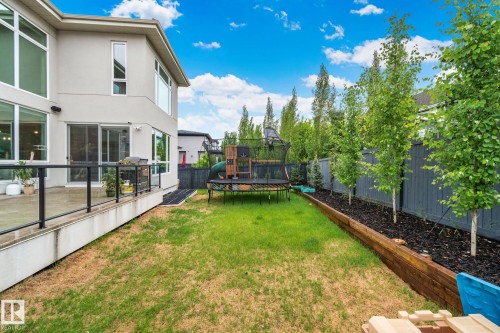 Expansive backyard featuring a manicured lawn, established trees, a wood-finish retaining wall, and a contemporary concrete patio with glass railings - 4509 Wingfield Bay Bay, Edmonton, AB 