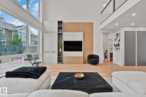 Contemporary living area featuring expansive floor-to-ceiling windows, light wood-finish flooring, and a two-story ceiling - 4509 Wingfield Bay Bay, Edmonton, AB 