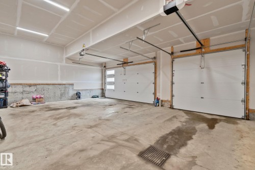 Two-car garage featuring a concrete floor, two overhead doors with automatic openers, and exposed drywall walls - 4509 Wingfield Bay Bay, Edmonton, AB 