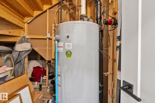 Water heater system featuring exposed plumbing lines, a circulation pump, and a matte black door handle - 4509 Wingfield Bay Bay, Edmonton, AB 