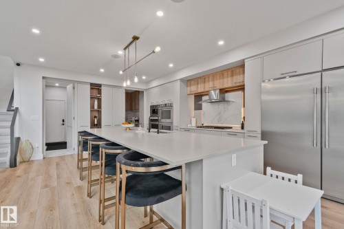 Modern kitchen featuring a large center island with seating, integrated stainless steel appliances, and wood-finish flooring - 4509 Wingfield Bay Bay, Edmonton, AB 